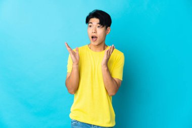 Genç Çinli bir adam mavi arka planda izole edilmiş ve yüzünde sürpriz bir ifade var.