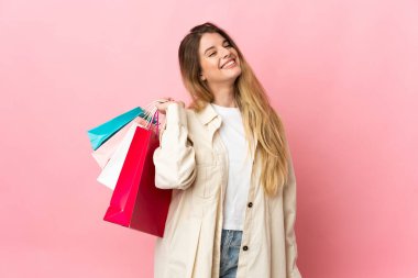 Alışveriş çantalı genç bir kadın pembe arka planda izole edilmiş alışveriş torbaları tutuyor ve gülümsüyor.