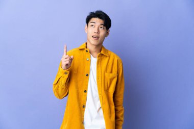 Mor arka planda izole edilmiş genç bir Çinli yukarı bakıyor ve şaşırıyor.