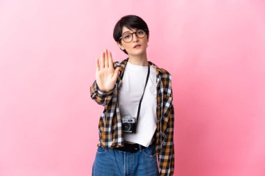 Pembe arka planda izole edilmiş genç fotoğrafçı kadın dur hareketi yapıyor.