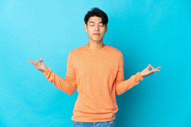 Zen pozisyonunda mavi arka planda izole edilmiş genç bir Çinli.