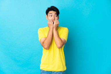 Mavi arka planda izole edilmiş genç bir Çinli gergin ve korkmuş bir şekilde elleriyle suni teneffüs yapıyor.