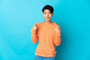 Mavi arka planda izole edilmiş genç bir Çinli baş parmak işareti yapıyor.