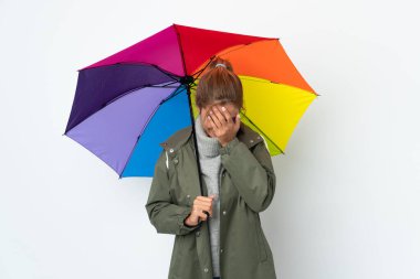 Beyaz arka planda şemsiye tutan genç bir kadın yorgun ve hasta bir ifadeyle izole edilmiş.