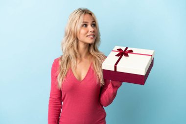 Elinde mavi arka planda izole edilmiş bir hediye tutan genç Rus kadın gülümserken yukarı bakıyor.