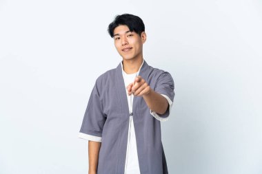 Beyaz arka planda izole edilmiş genç Çinli adam mutlu bir ifadeyle ön tarafı işaret ediyor.