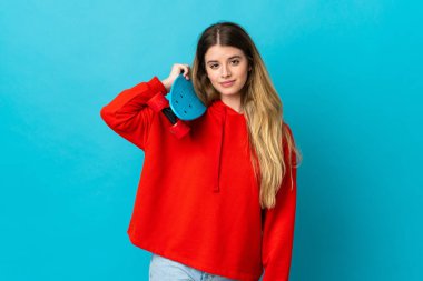 Genç sarışın kadın mavi arka planda tek başına paten kayıyor.