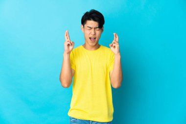 Genç Çinli adam mavi arka planda izole edilmiş ve şans diliyor.