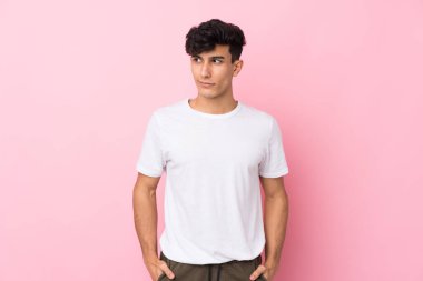Arjantinli genç bir adam pembe arka planda duruyor ve yan tarafa bakıyor.