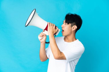 Mavi arka planda izole edilmiş genç bir Çinli megafonla bir şey duyurmak için bağırıyor.