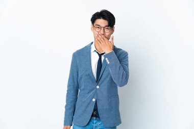 Genç Çinli iş adamı beyaz arka planda izole edilmiş mutlu ve gülümseyen ağızlarını eliyle kapatıyor.