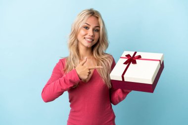 Elinde mavi arka planda izole edilmiş bir hediye tutan genç Rus kadın.