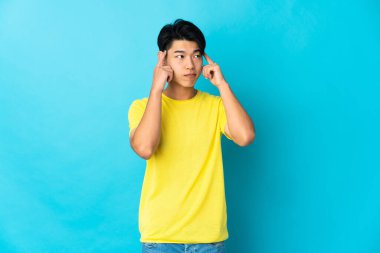 Genç Çinli bir adam mavi arka planda izole edilmiş. Şüpheleri ve düşünceleri var.