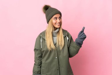 Pembe arka planda izole edilmiş, kış şapkalı genç kadın harika bir fikre işaret ediyor.