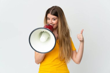 Beyaz arka planda izole edilmiş genç sarışın bir kadın megafondan bir şey duyurmak için bağırıyor ve başparmağını kaldırıyor.