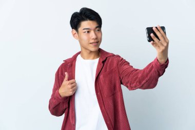 Beyaz arka planda izole edilmiş genç bir Çinli cep telefonuyla selfie çekiyor.
