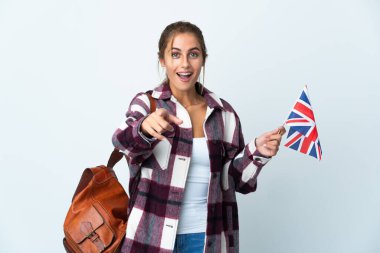 Beyaz arka planda izole edilmiş İngiliz bayrağı tutan genç bir kadın şaşırmış ve ön tarafı işaret ediyor.