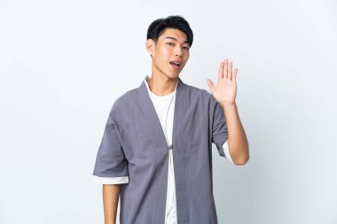 Beyaz arka planda izole edilmiş genç bir Çinli mutlu bir ifadeyle selamlıyor.