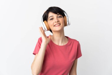Kısa saçlı bir kadın beyaz arka planda müzik dinliyor.