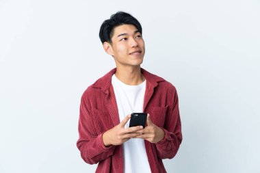 Genç Çinli bir adam beyaz arka planda cep telefonu kullanarak izole edilmiş.