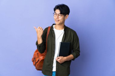 Mor arka planda izole edilmiş genç bayan bir ürünü sunmak için yan tarafı işaret ediyor.