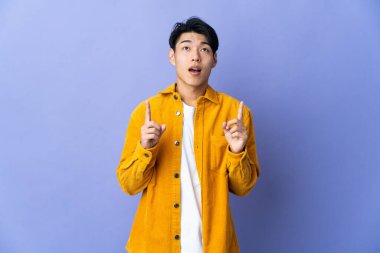 Mor arka planda izole edilmiş genç bir Çinli şaşırmış ve yukarı bakıyor.