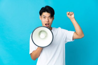 Mavi arka planda izole edilmiş genç bir Çinli megafonla bir şey duyurmak için bağırıyor.
