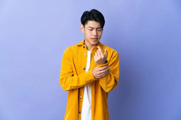 手の痛みに苦しんで紫色の背景に隔離された若い中国人男性 — ストック写真