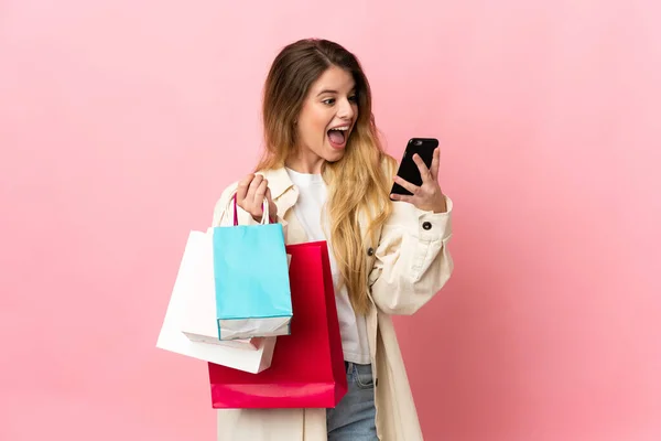 提着购物袋 背景为粉色的年轻女子拿着购物袋 用手机给朋友留言 — 图库照片