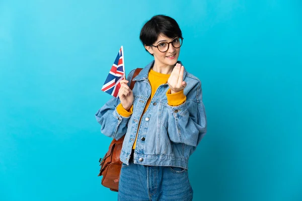 Woman holding an United Kingdom flag over isolated background inviting to come with hand. Happy that you came