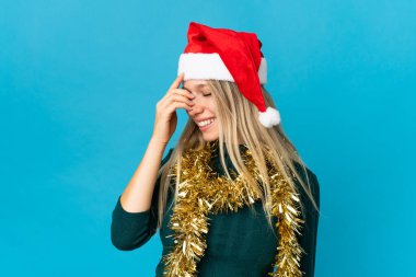 Mavi arka planda izole edilmiş, Noel şapkalı kadın gülüyor.