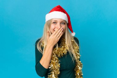 Mavi arka planda izole edilmiş bir Noel şapkası olan mutlu ve gülümseyen bir kadın.