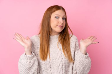 Genç kızıl saçlı kadın pembe arka planda şüpheli hareketler yapıyor.