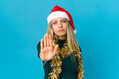 Mavi arka planda izole edilmiş noel şapkalı kadın dur hareketi yapıyor.