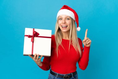 Noel şapkalı bir kadın mavi arka planda izole edilmiş bir hediyeyle harika bir fikre işaret ediyor.