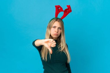 Mavi arka planda izole edilmiş noel şapkalı bir kadın olumsuz ifadeyle baş parmağını aşağı gösteriyor.