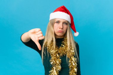 Mavi arka planda izole edilmiş noel şapkalı bir kadın olumsuz ifadeyle baş parmağını aşağı gösteriyor.