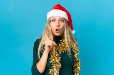 Mavi arka planda izole edilmiş Noel şapkalı kadın parmağını kaldırarak çözümü anlamaya çalışıyor.