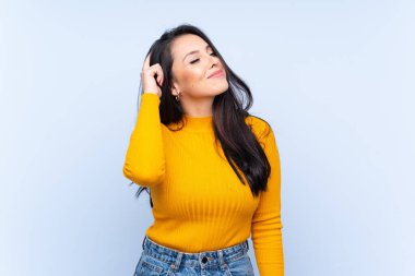 İzole edilmiş mavi arka plan üzerinde genç Kolombiyalı kızın şüpheleri ve kafa karıştırıcı bir yüz ifadesi var.