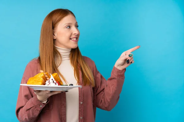 Young Redhead Woman Holding Waffles Isolated Background Pointing Side Present — Stock Photo, Image