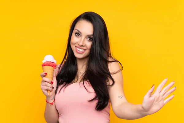 Joven Colombiana Sosteniendo Helado Corneta Sobre Fondo Amarillo Aislado Saludando —  Fotos de Stock