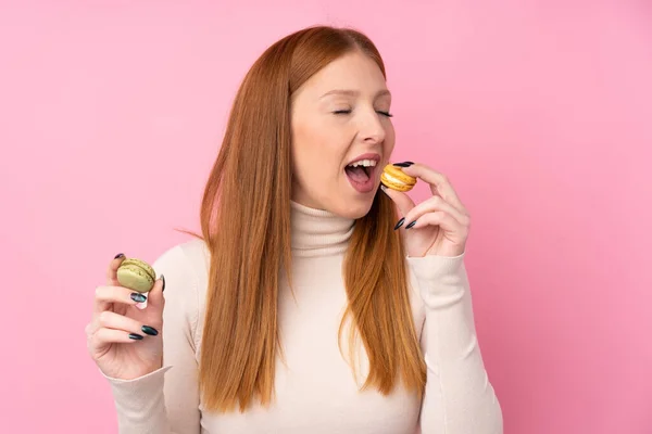 一位红头发的年轻女子 身披粉红色的孤立背景 手里拿着五颜六色的法国金银花 正在吃着 — 图库照片