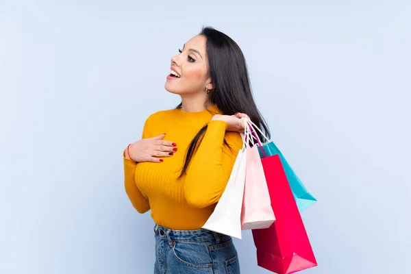 Joven Colombiana Sobre Fondo Azul Aislado Sosteniendo Bolsas Compras Sonriendo —  Fotos de Stock