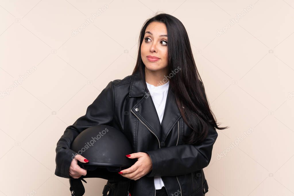 Young Colombian girl holding a motorcycle helmet over isolated background standing and looking to the side