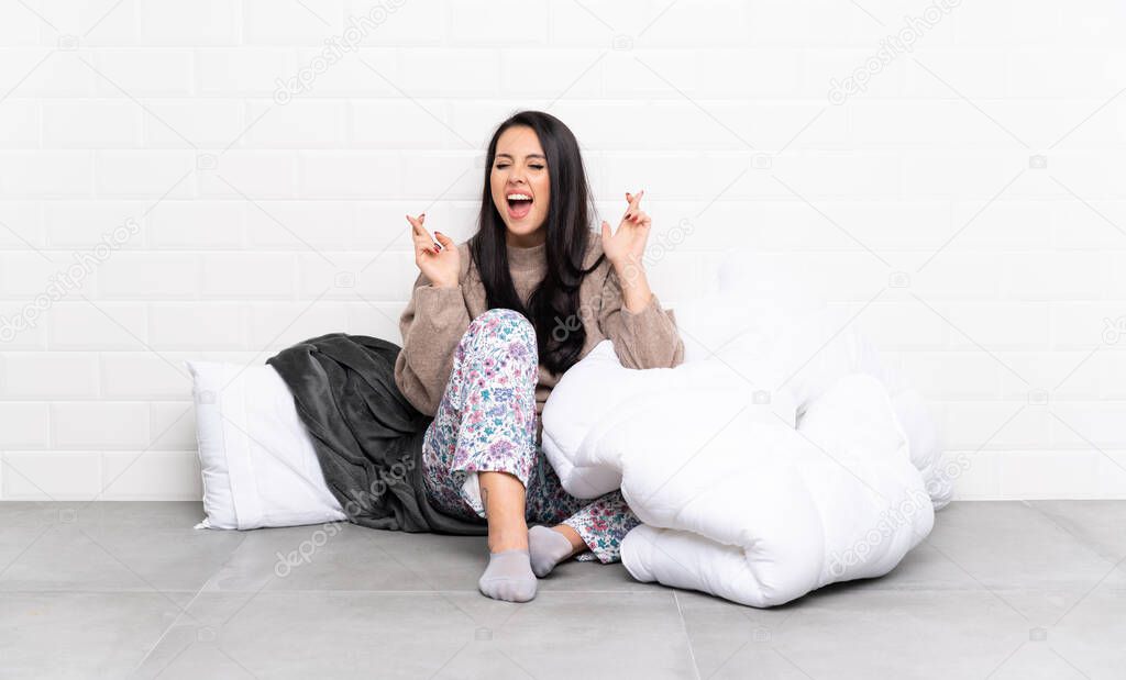 Young Colombian girl in pajamas at indoors with fingers crossing