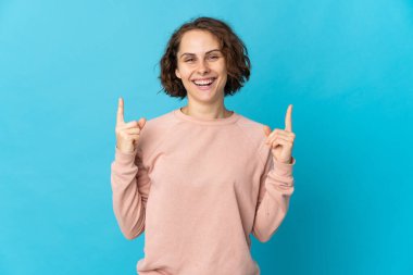 Genç İngiliz bisikletçi kadın, beyaz arka planda izole edilmiş mutlu ve gülümseyen ağızlarını eliyle kapatıyor.