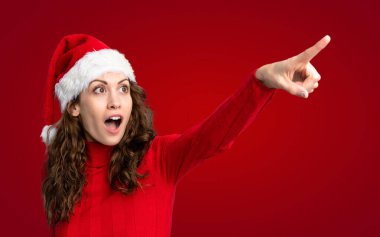 İzole edilmiş kırmızı arka planda Noel şapkası takan kız.