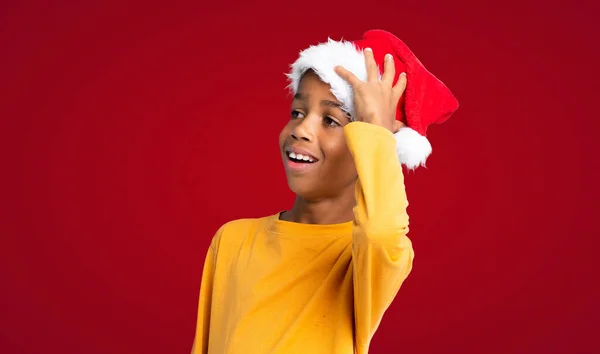 戴着圣诞礼帽的非洲裔美国男孩已经意识到了一些事情 并打算在红色背景下寻找解决方案 — 图库照片