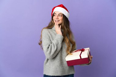 Noel şapkalı kız elinde hediyeyle beyaz arka planda beş parmaklı sayım yapıyor.