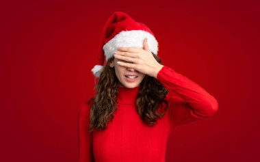 İzole edilmiş kırmızı arka planda Noel şapkası takan kız.